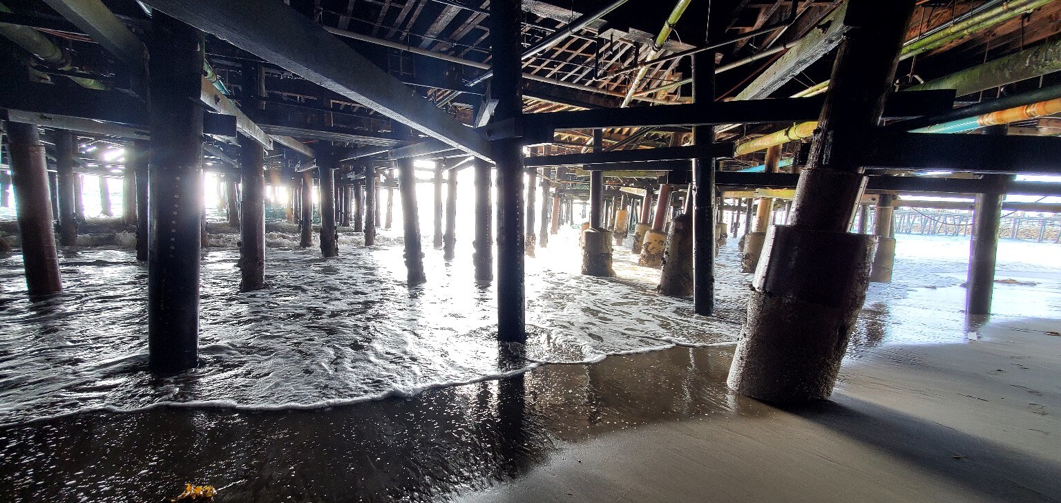 Waves moving between the wooden supports beneath a South Bay pier